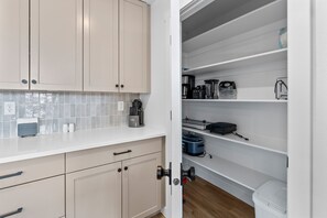 A kitchen with beige cabinets, a white countertop, and a white tiled backsplash. There are various appliances and utensils on the shelves. - Zion Cliffside Retreat l Gem for Relaxation (Hurricane)