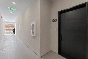 Un pasillo con una puerta marcada '103', un letrero de salida y vistas de un paisaje desértico.