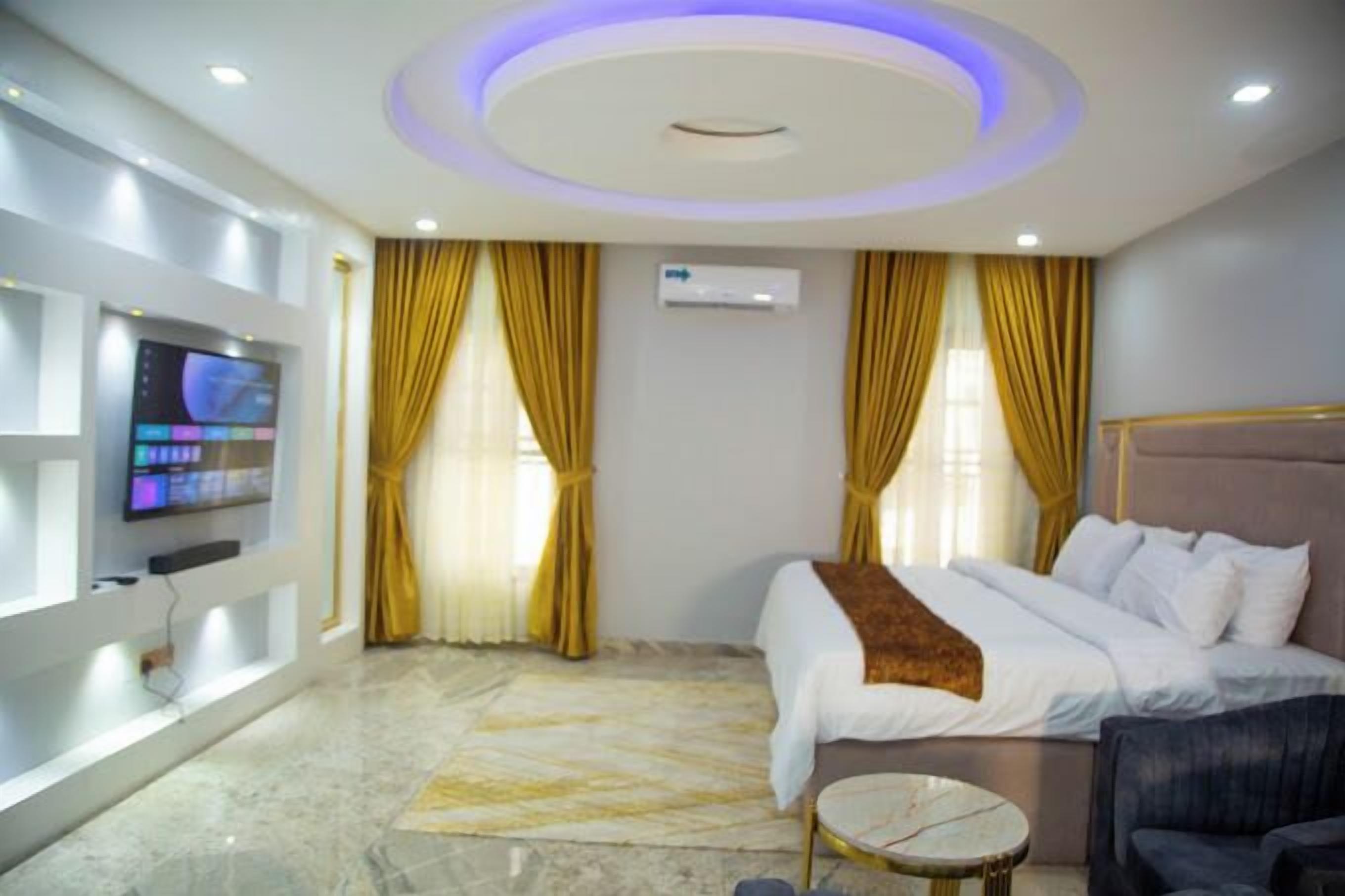 Une chambre d’hôtel avec un lit, un téléviseur fixé au mur, une table ronde et un plafond doté d’un éclairage circulaire.