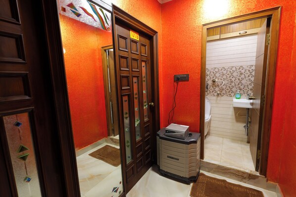 A hallway with a wooden door marked "EXIT," a small desk with a computer, and a bathroom with a sink and toilet. - SBHS Homestay - Neeladri  (Tirupati)