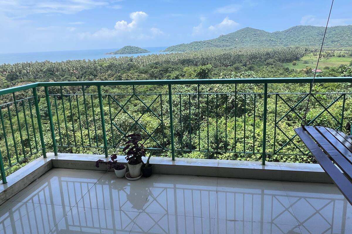 A balcony with a green metal railing, a tiled floor, and potted plants.