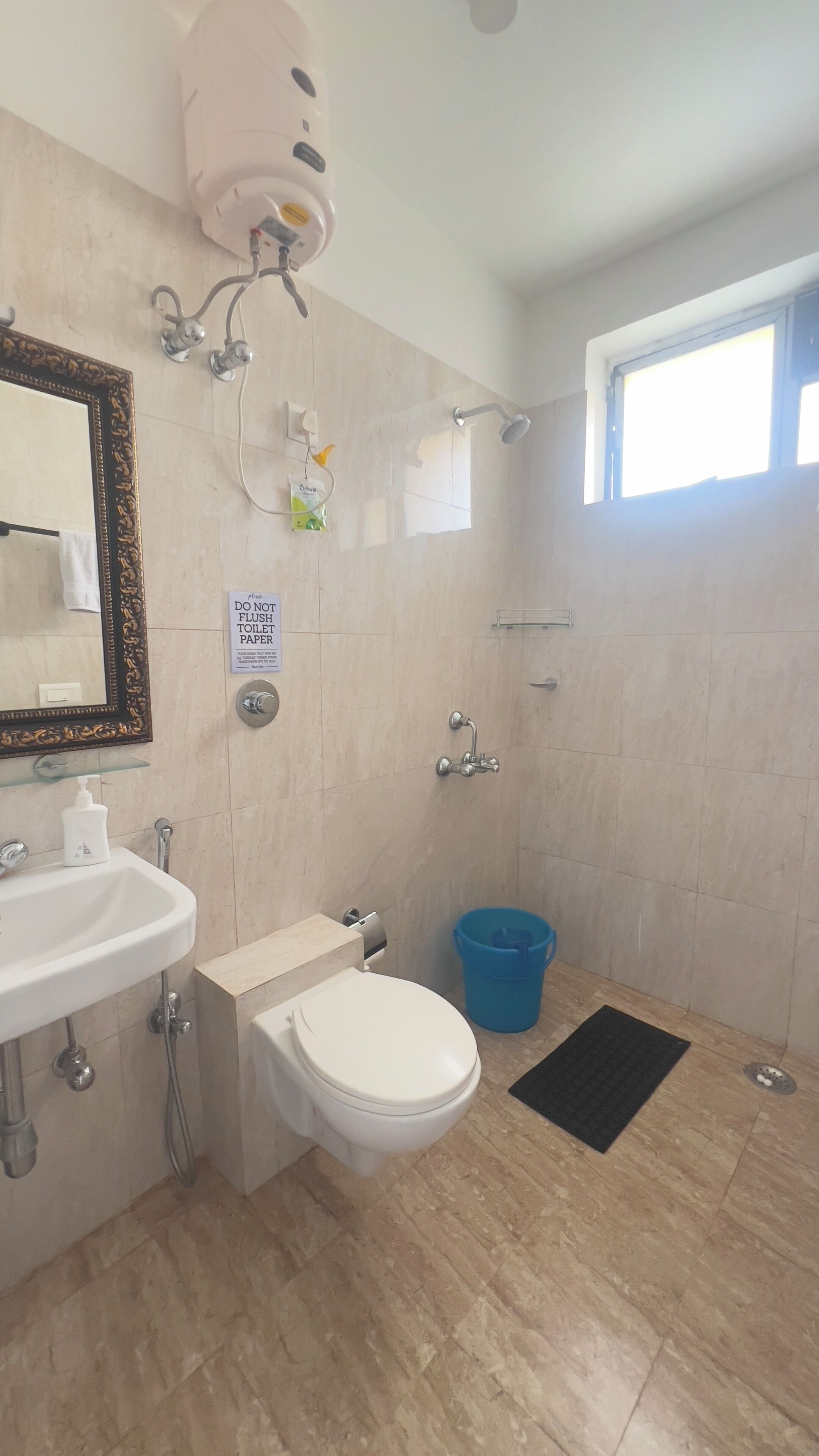 Un baño con inodoro, lavamanos, ducha y un cubo azul.