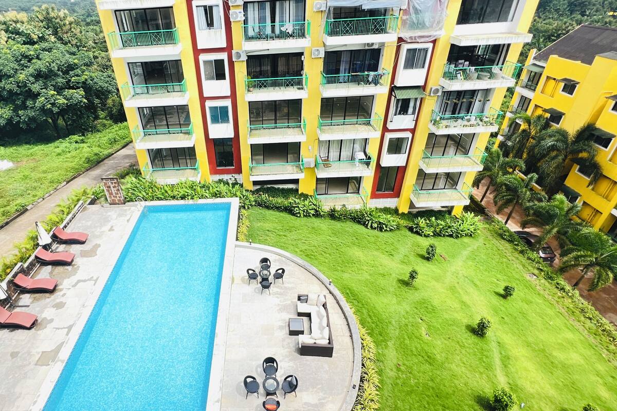 A multi-story hotel with a swimming pool, outdoor seating, and lush greenery.