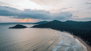 A coastal landscape with a beach, a small island, and mountains in the background. - The Nautical Nest (Canacona)