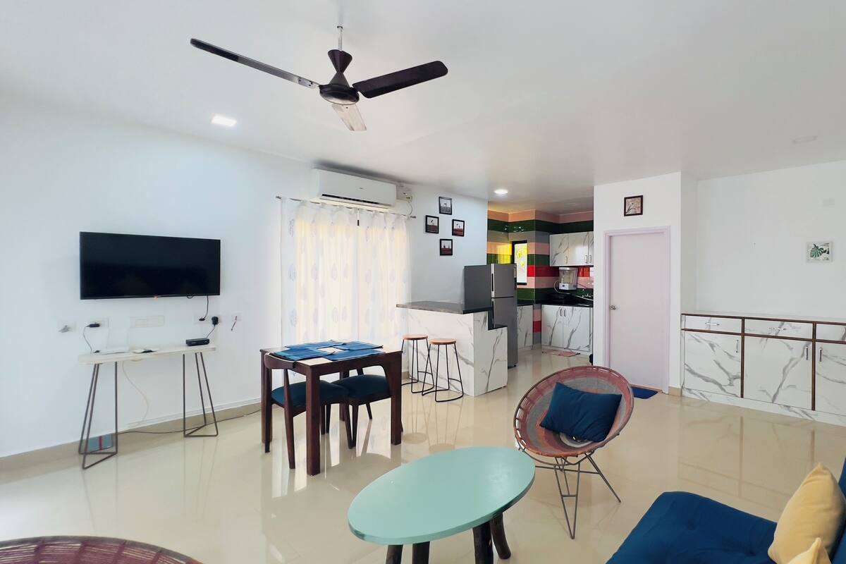A modern living room with a TV, a dining area, and a kitchen.