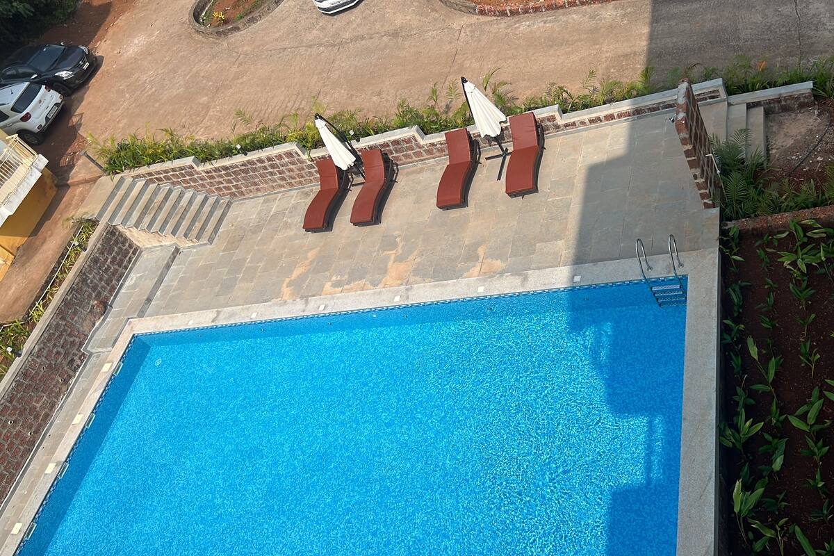A rectangular swimming pool with a tiled deck and lounge chairs.