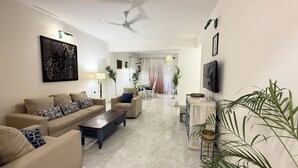 A modern living room with a sofa set, a coffee table, a TV, and a ceiling fan. - The Nautical Nest (Canacona)
