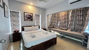 A bedroom with a large bed, a bench with cushions, floral curtains, and framed artwork on the walls. - The Nautical Nest (Canacona)