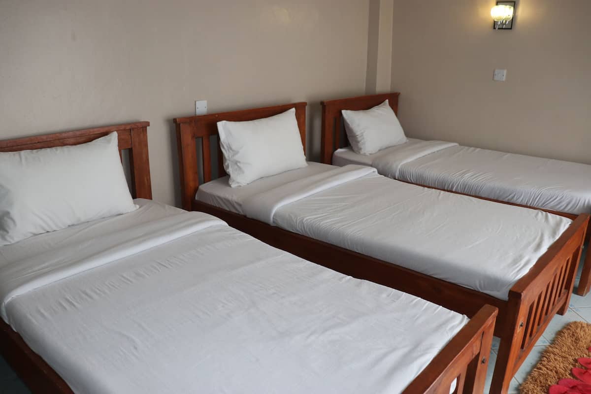 Three single beds with wooden frames and white bedding in a room with beige walls and a light fixture.