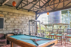 A pool table with a green felt surface, surrounded by wicker chairs and a wooden table.