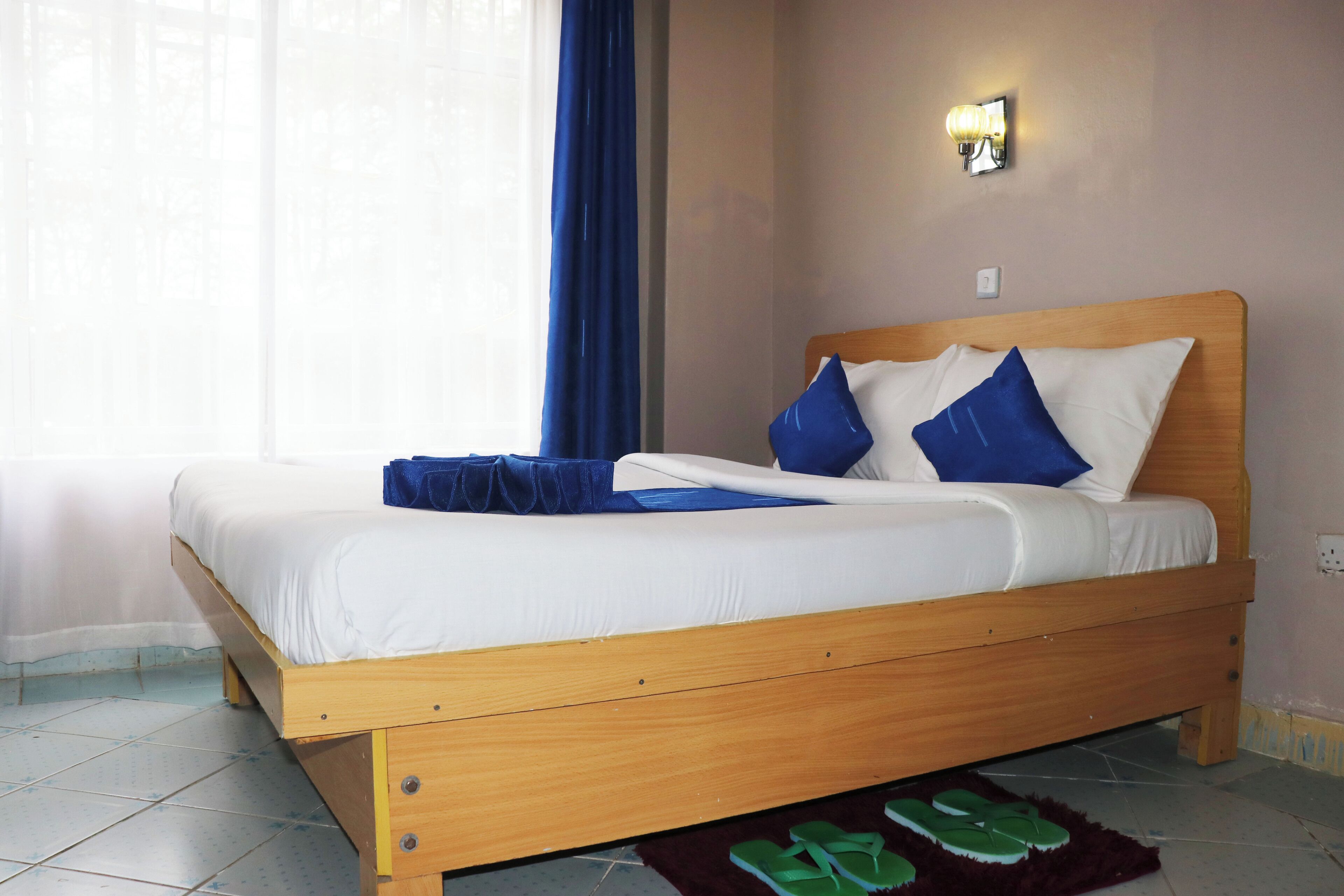 Una cama bien hecha con estructura de madera, ropa de cama blanca y almohadas azules.