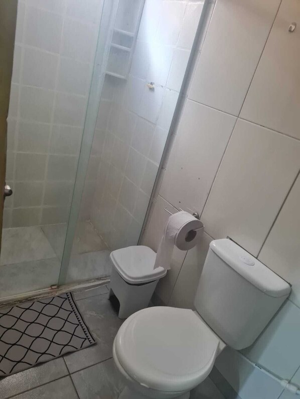 A small, compact bathroom with a toilet, a glass shower enclosure, and a toilet paper holder. - Pousada v. Porto (Ipojuca)