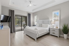 A bedroom with a bed, a TV, a nightstand, a potted plant, and a sliding glass door leading to a balcony.