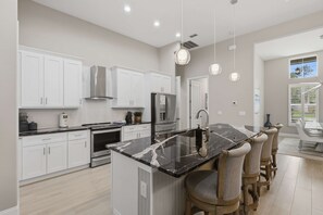 Una cocina moderna con gabinetes blancos, una isla de mármol e iluminación colgante.