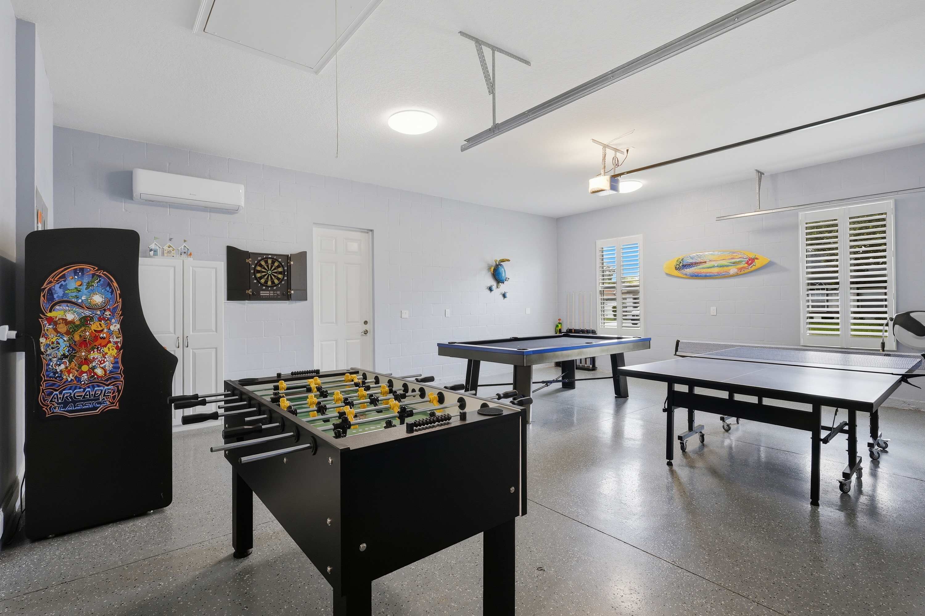 A room with a foosball table, ping pong table, dartboard, and a pool table.