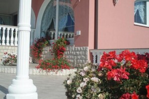 Flower arrangements adorn the exterior of this building, featuring a pink facade and white balcony railing.