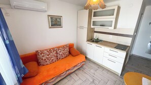 Ein kompakter Wohnbereich mit Sofa, Küchenzeile und Deckenleuchte.