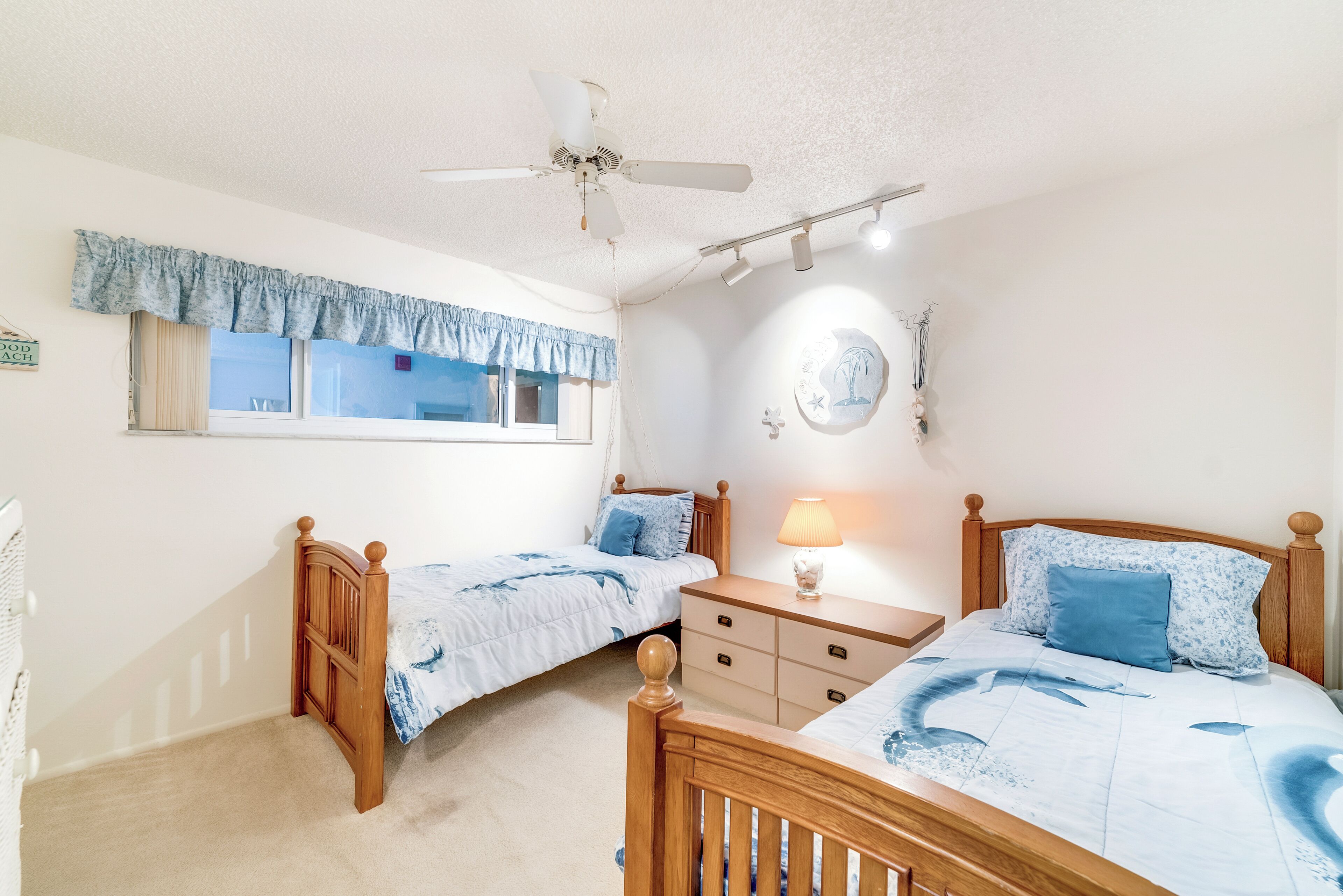 A bedroom with two single beds, a ceiling fan, a bedside table with a lamp, and a window with curtains.