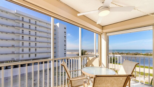 Ein Balkon mit Glastisch und Stühlen, mit Blick auf einen Strand und ein Hochhaus.