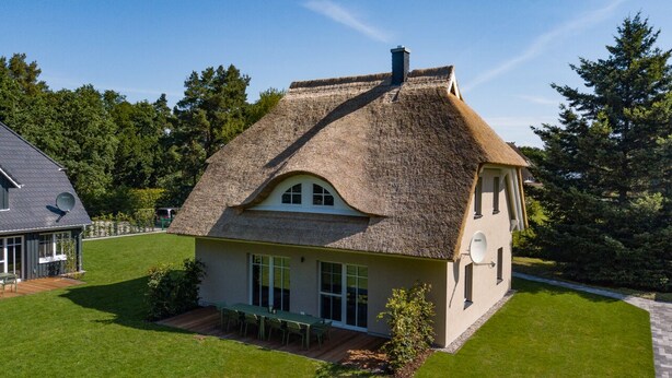 Een huis met rieten dak, grote ramen en een verzorgd gazon.