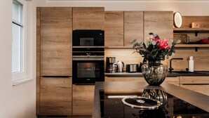 Een moderne keuken met houten kastjes, een ingebouwde oven, een magnetron, een koffiezetapparaat en een bloevas op het aanrecht.