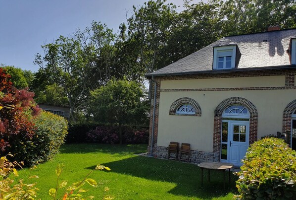 A two-story house with a brick facade, a white door, and a small garden with a lawn and various plants. - HOUSE COTE NORMANDE NEAR THE BEACHES (Sassetot-le-Mauconduit)