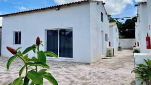 A white building with a tiled roof, a sliding glass door, and a small window. There are potted plants and a fire extinguisher mounted on the wall. - Casa Les Deux R da Lagoa (Jijoca de Jericoacoara)
