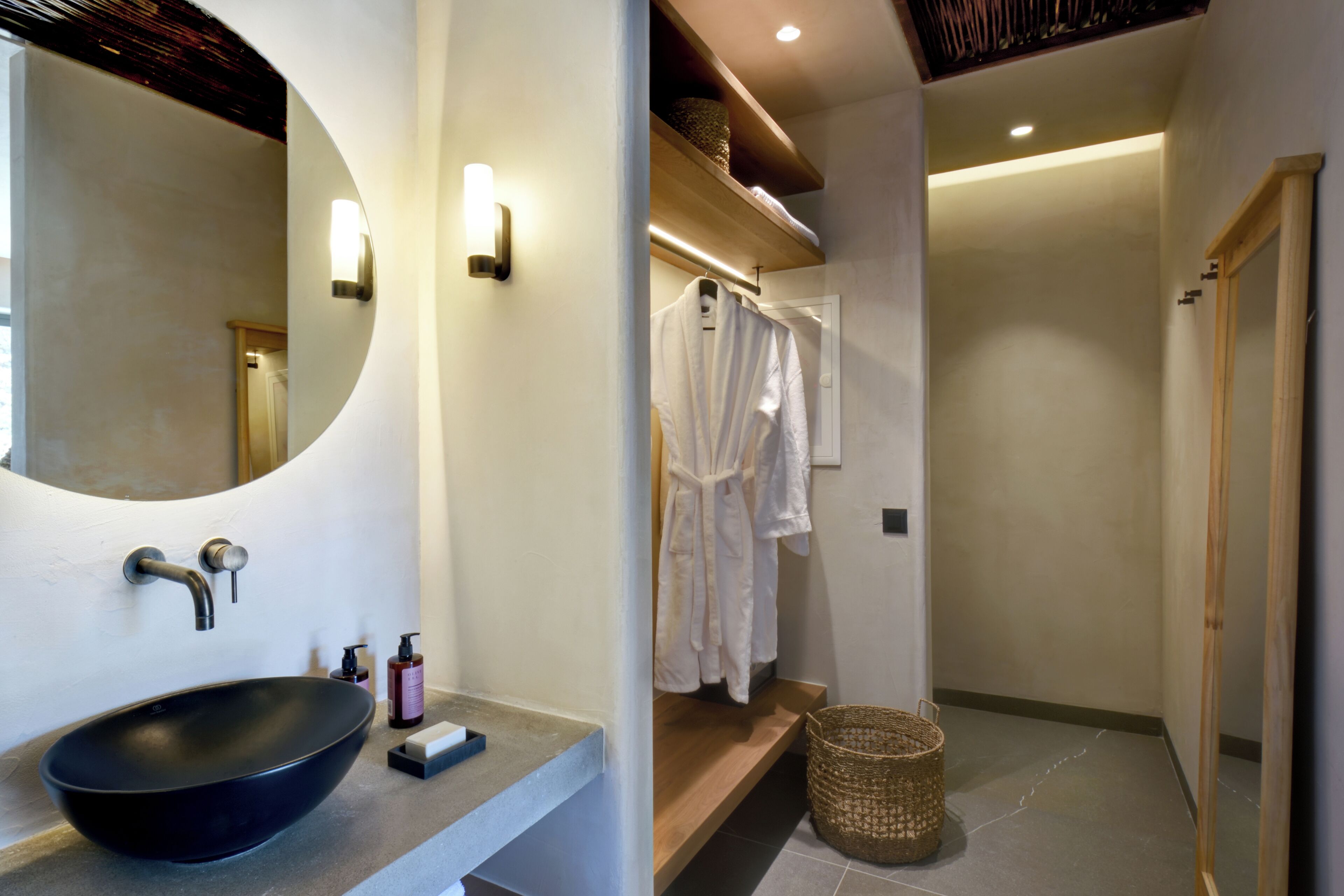 A modern bathroom with a round mirror, a black vessel sink, and a wooden shelf above the sink.
