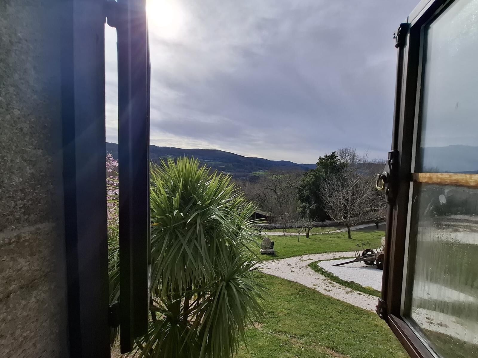 A view from a window overlooking a garden with a pathway, a lawn, and distant hills. - Val Fresco Suites & Relax (A Estrada)