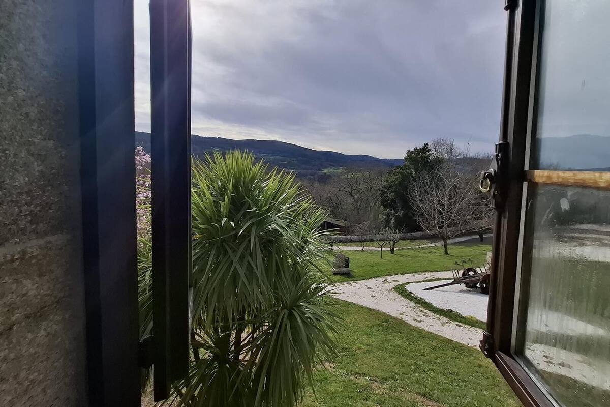 A view from a window overlooking a garden with a pathway, a lawn, and distant hills.