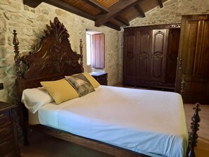 A bedroom with a large wooden bed, a wardrobe, and a stone wall. - Val Fresco Suites & Relax (A Estrada)
