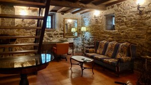 A rustic room with stone walls, a wooden ceiling, a sofa, a coffee table, and a chair. - Val Fresco Suites & Relax (A Estrada)