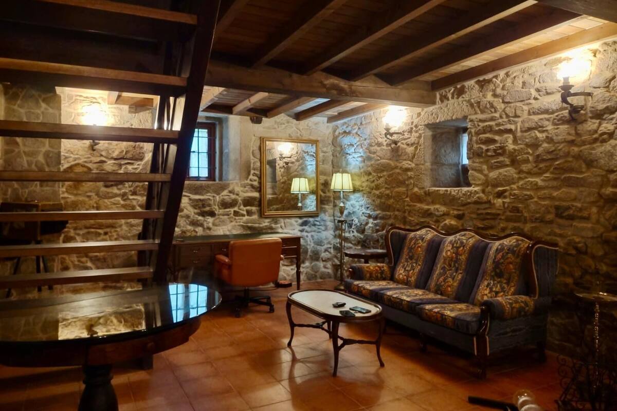 A rustic room with stone walls, a wooden ceiling, a sofa, a coffee table, and a chair.
