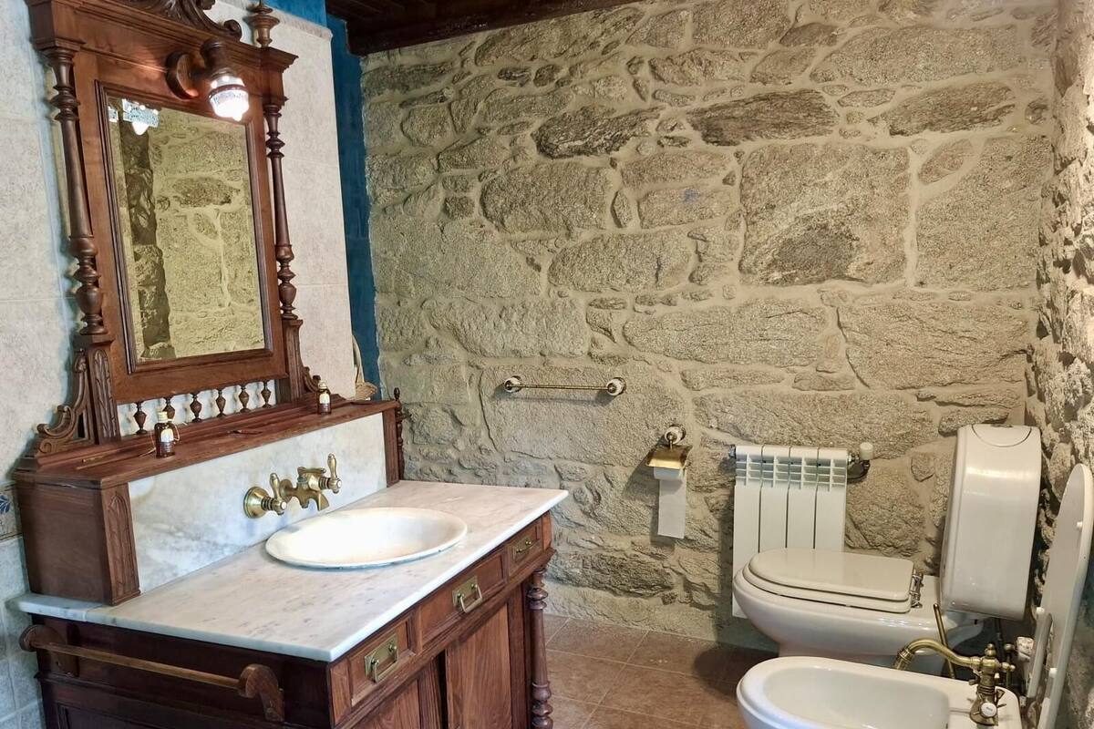 A bathroom with a stone wall, a wooden vanity with a mirror, a sink, and a toilet.