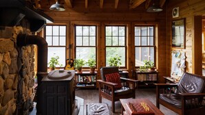 A cozy cabin interior with a stone wall, wooden beams, a fireplace, a guitar, a chessboard, and a bookshelf. - ADA Cabin, Queen Bed, Double Bed, Private Bath (Greenville)