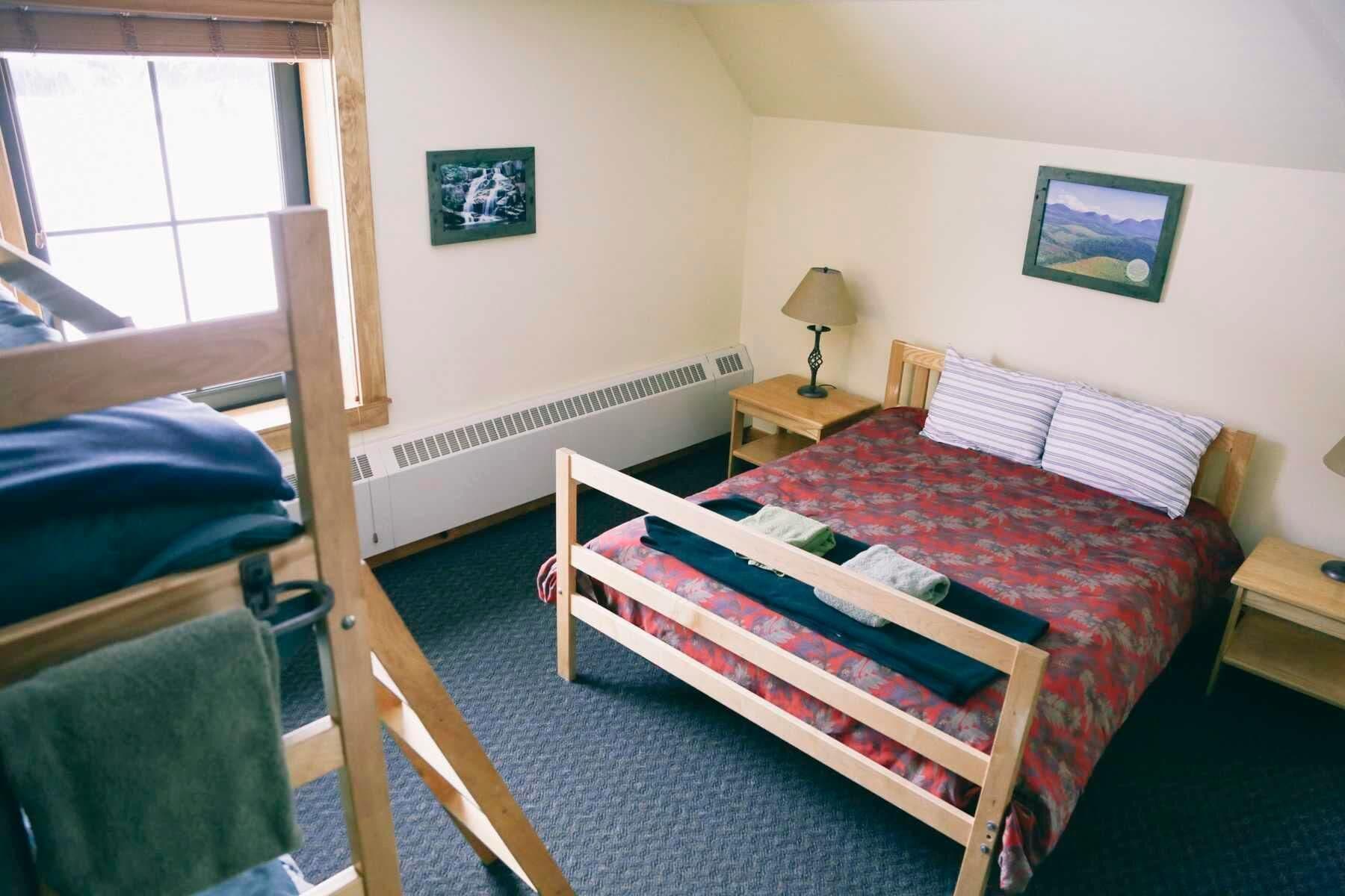 Ein Zimmer mit einem Etagenbett, einem kleinen Nachttisch mit Lampe und zwei gerahmten Bildern an den Wänden.