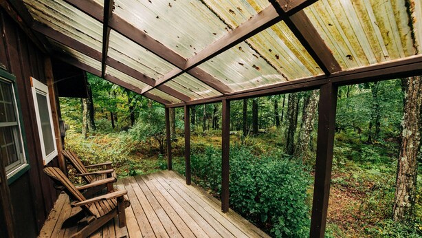 Una terraza de madera con techo metálico que da a un área boscosa.