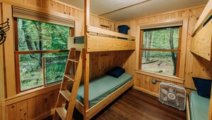 Una cabaña de madera con literas, una escalera y un ventilador.