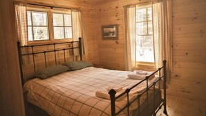 A wooden cabin bedroom with a bed, checkered curtains, and a framed picture on the wall. - Comfy Lakeside Cabin:  All Meals, Canoes, & Kayaks Included, Shared Sauna (Greenville)