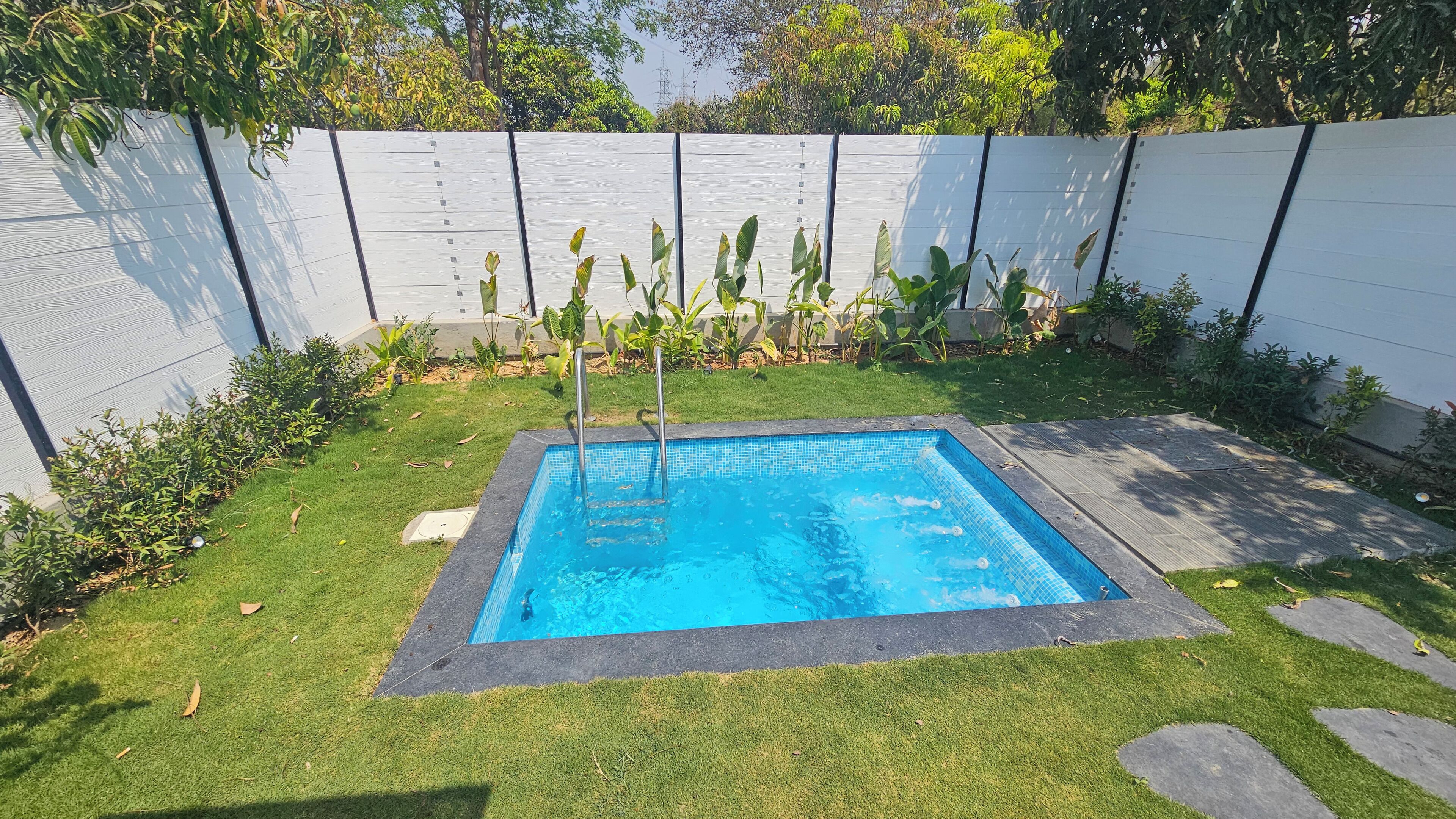 Una piscina rectangular con borde de azulejos, rodeada por un césped cuidado y un muro blanco bajo.