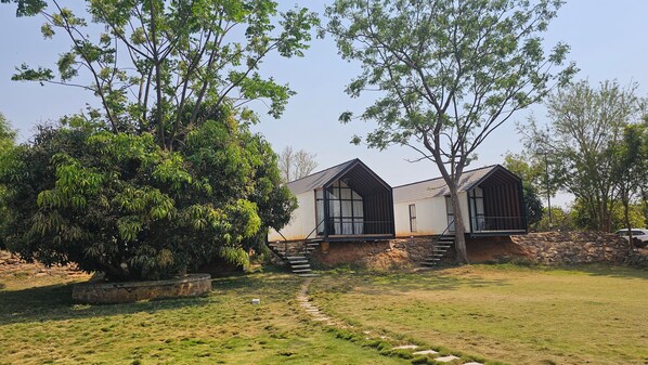 A two-story building with a stone foundation and a wooden roof. There is a stone staircase leading to the entrance. - Aura Farms - Private Pool Cottages (Ramanagara)