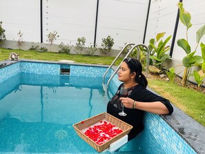 A swimming pool with a tiled edge, a glass of red liquid, and a basket of red flower petals. - Aura Farms - Private Pool Cottages (Ramanagara)