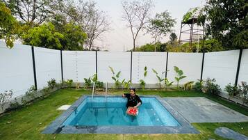 A swimming pool with a person holding a box of items, surrounded by a white fence and greenery.