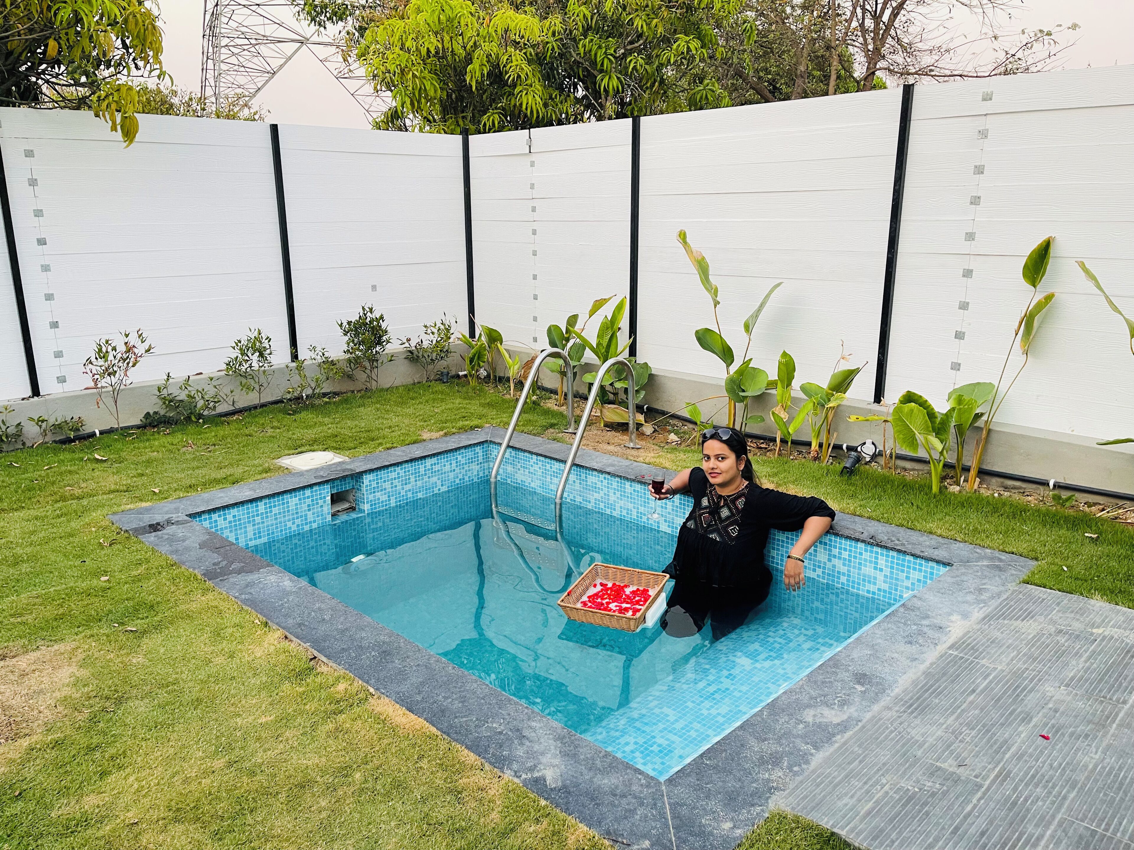 Una piscina con borde de azulejos, rodeada de césped y plantas.