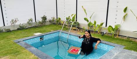 Una piscina con borde de azulejos, rodeada de césped y plantas.