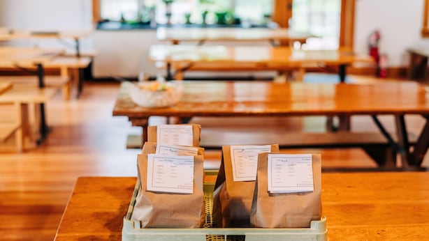 Un café avec des tables et des bancs en bois, et des sacs en papier étiquetés, posés sur une table.