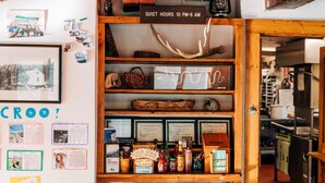 Un intérieur chaleureux avec une étagère en bois où sont exposés divers objets, un panneau indiquant les heures de silence, et des certificats encadrés accrochés au mur.
