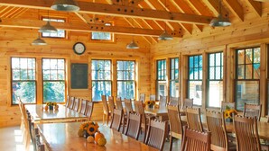 A large wooden dining table surrounded by chairs in a spacious room with high ceilings and large windows. - Cabin, two queen beds with shared bathroom (Greenville)