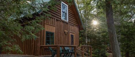 A rustic cabin with a wooden exterior, a porch with chairs, and a signboard.