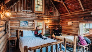 A log cabin with two beds, a wooden ceiling, and a sign that reads "Lost Canoe Lake".